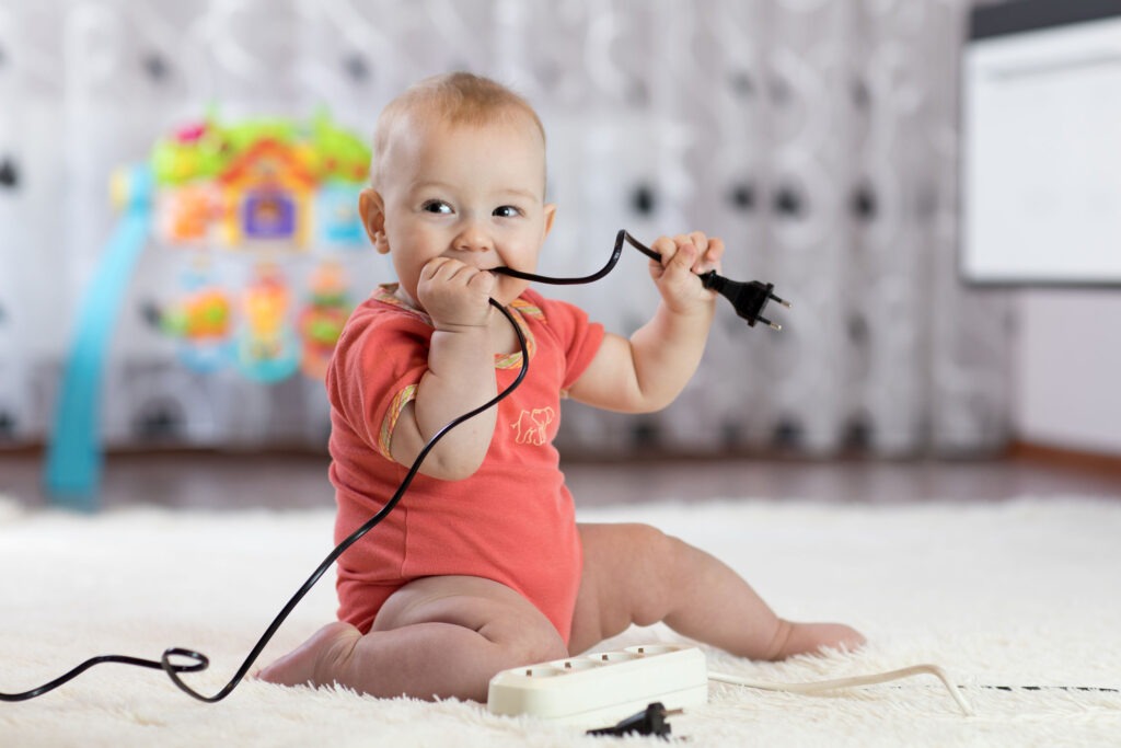 baby sitting up chewing on an unplugged electrical cord