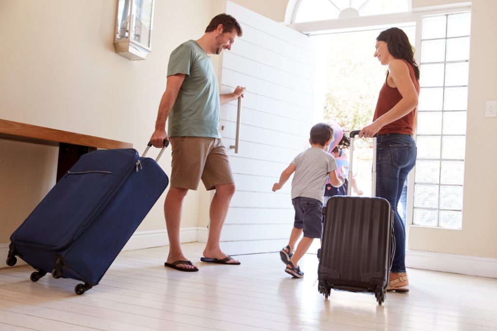 A mother, father and child walk out the door of their home with luggage