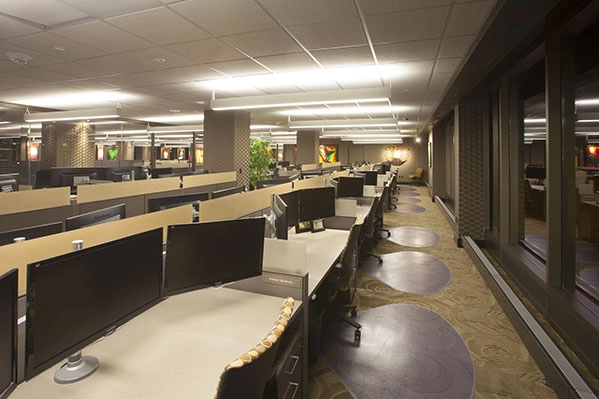 long desk with a row of computer monitors with office lighting on the ceiling